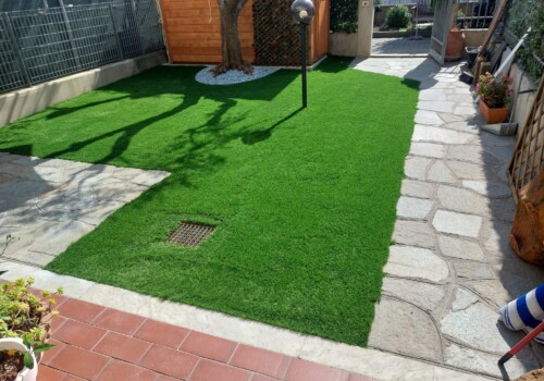 Prato sintetico con ingresso in pietra e casetta da giardino in legno