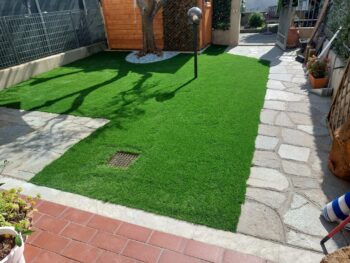 Prato sintetico con ingresso in pietra e casetta da giardino in legno
